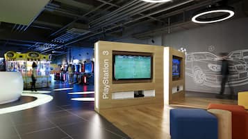 A PlayStation 3 gaming area with multiple screens, arcade games, and modern seating.