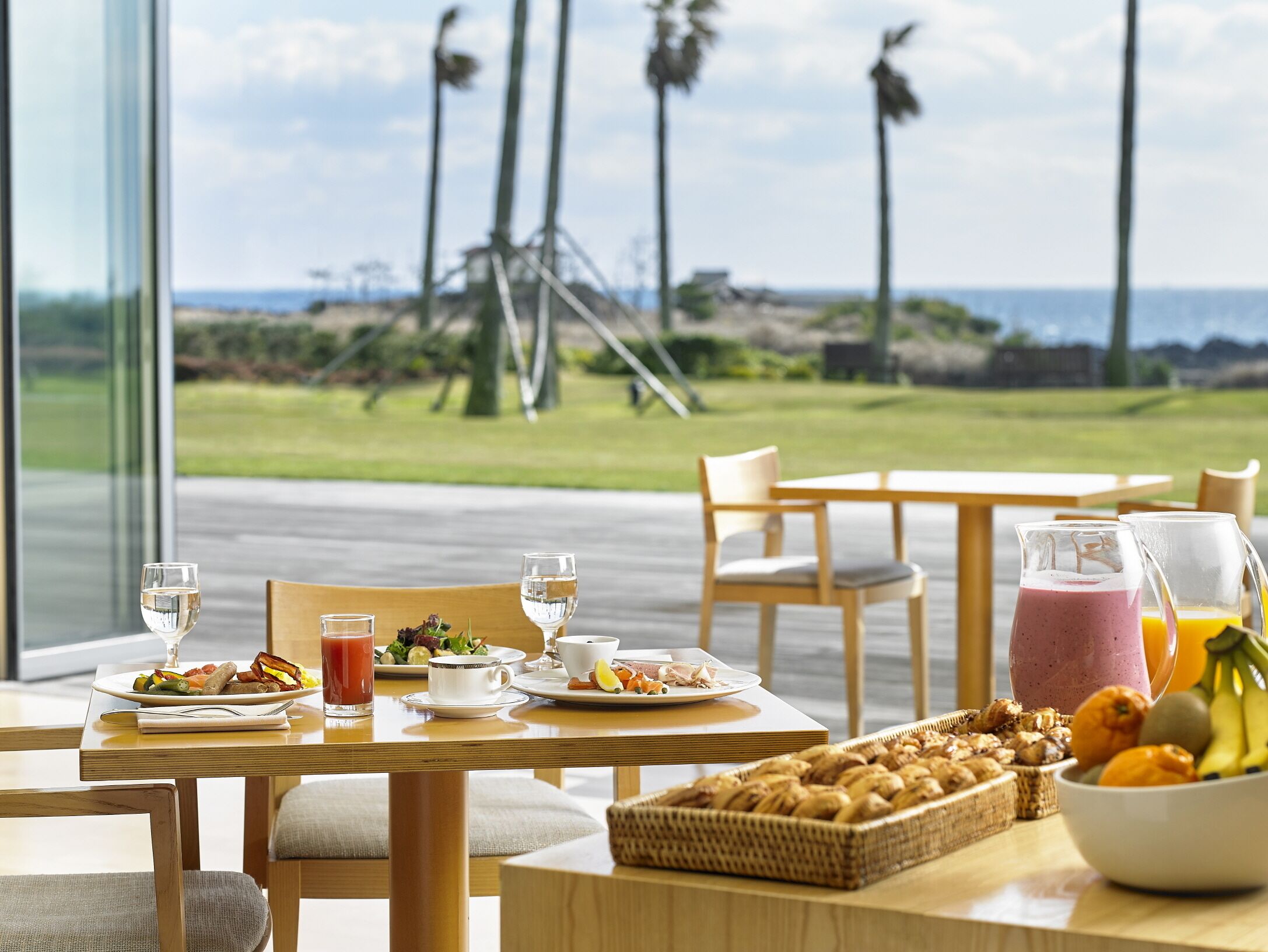 Un comedor con vista al océano, una mesa dispuesta para el desayuno y una cesta de pasteles.