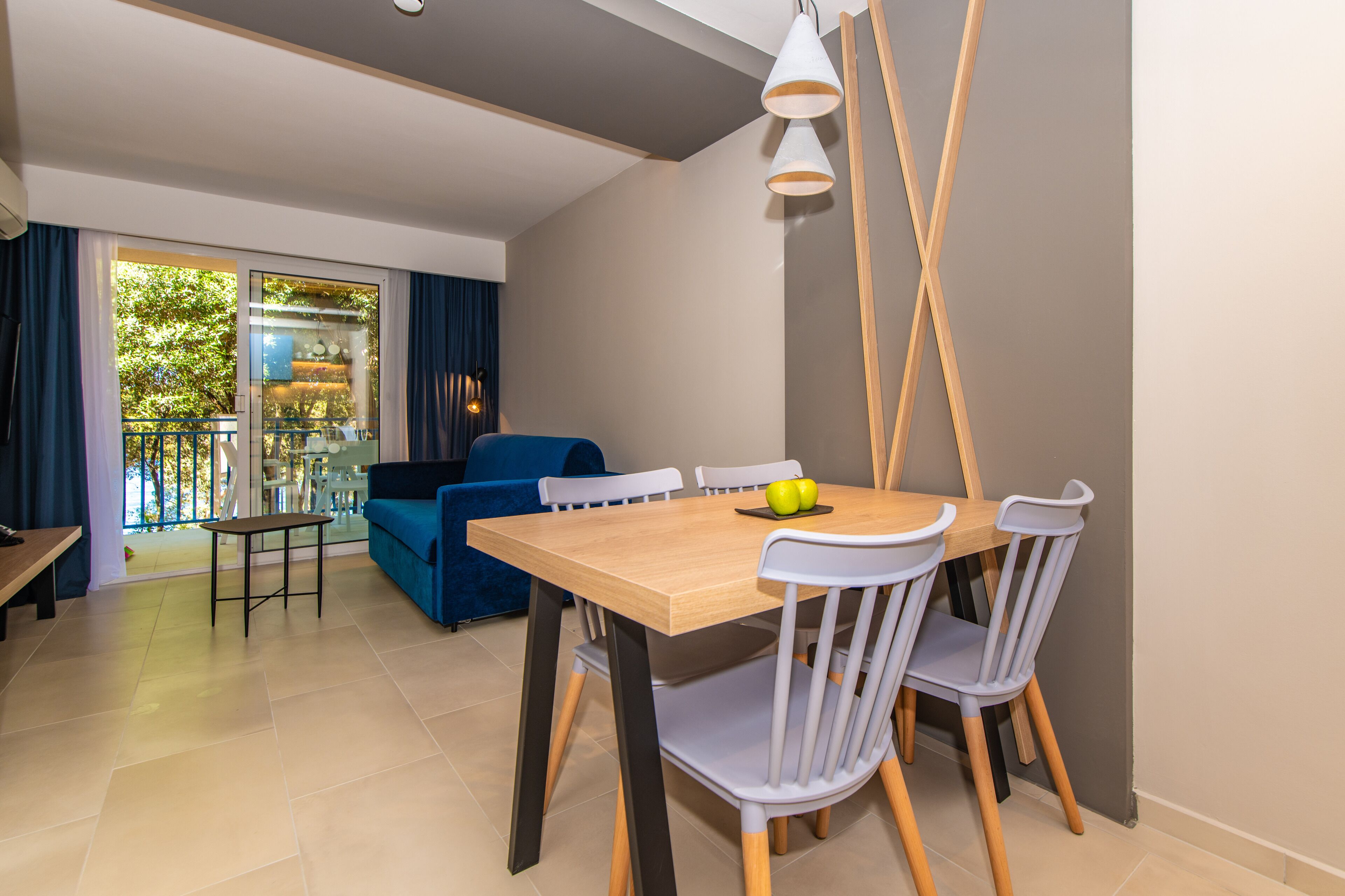 A modern dining area with a wooden table and white chairs, a blue sofa, and a balcony with a glass door.