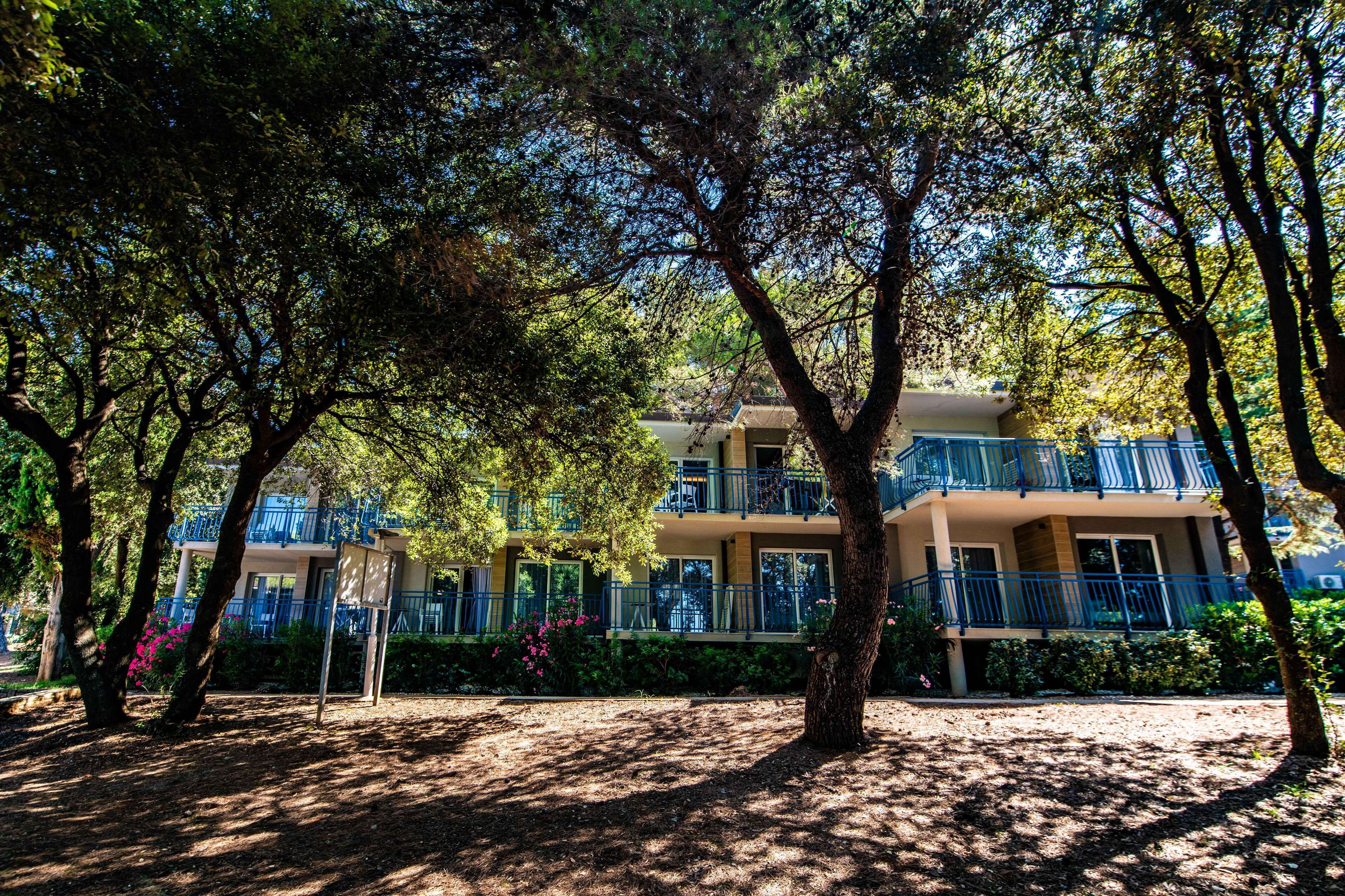 A multi-story building with balconies, surrounded by trees and greenery.