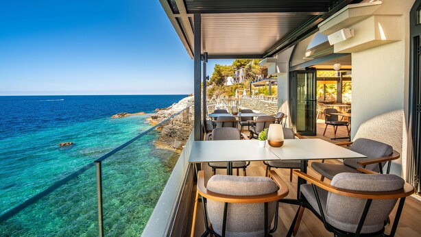 A balcony with a table and chairs overlooking a coastal area with clear blue water and rocky shore. - Arena Verudela Beach Apartments (Pula)