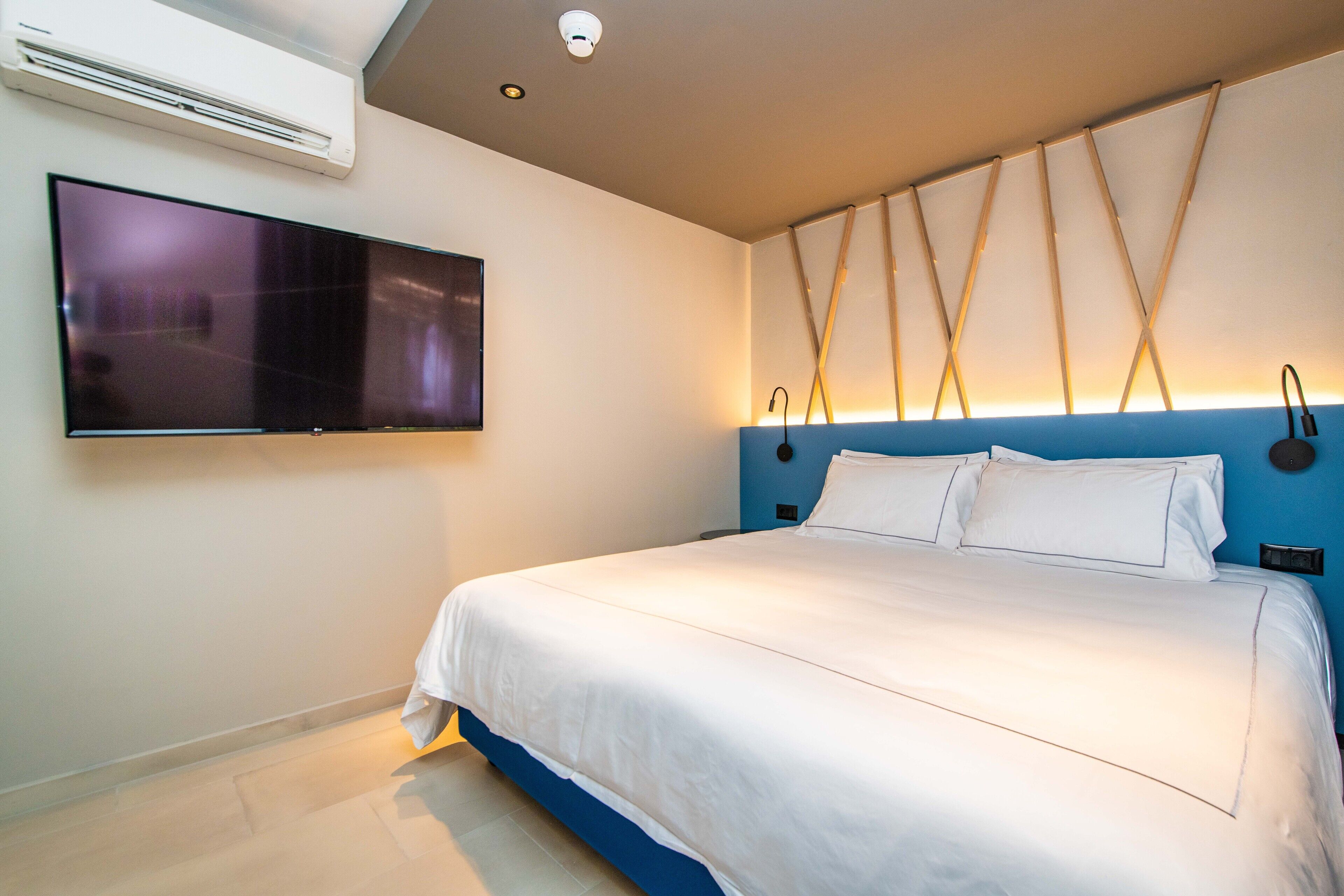 Una camera d'hotel moderna con un letto grande, una TV a schermo piatto montata e un design del soffitto originale.