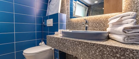 Une salle de bain moderne avec des carreaux bleus, des toilettes blanches, un comptoir en granit et un lavabo surmonté d’un miroir.