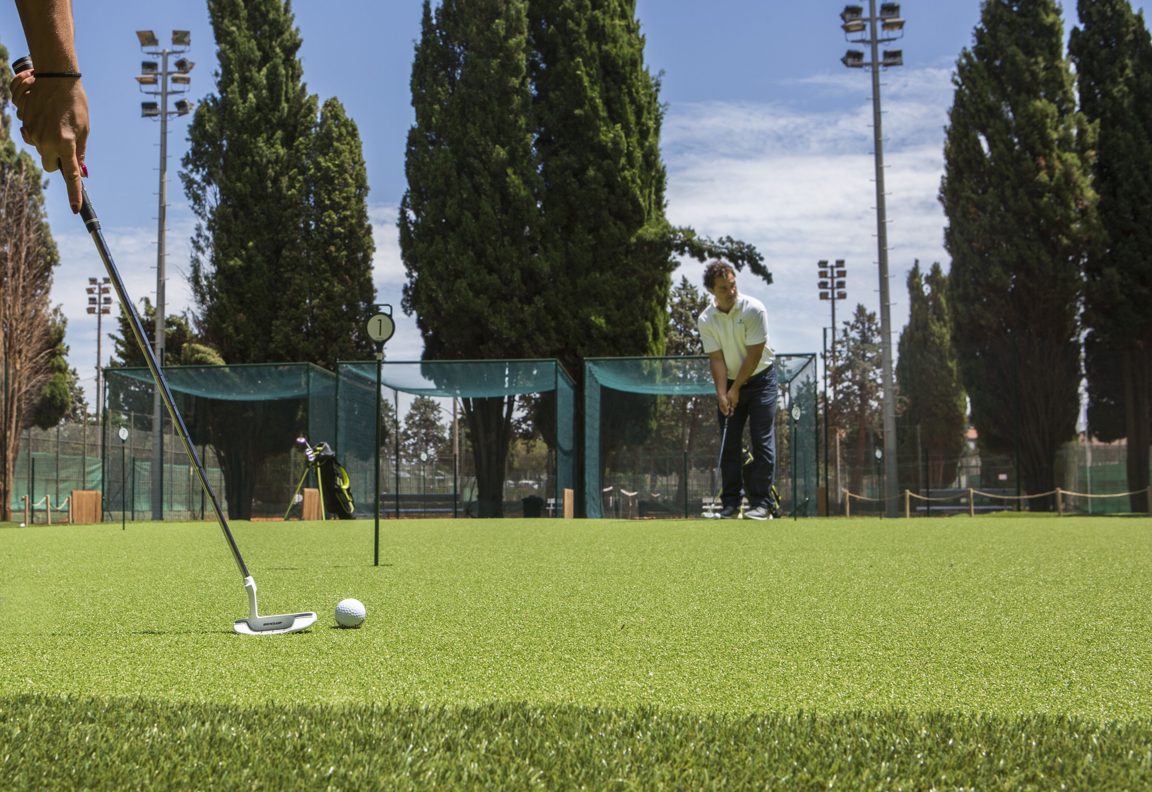 Campo de golf con un green de putting, una pelota de golf y un putter.