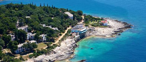 Vue aérienne d’une zone résidentielle côtière, avec des maisons, une plage et une côte rocheuse.