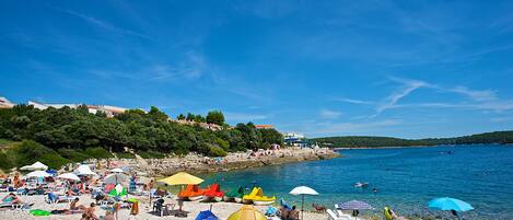 A beach with people sunbathing, tents, and boats.