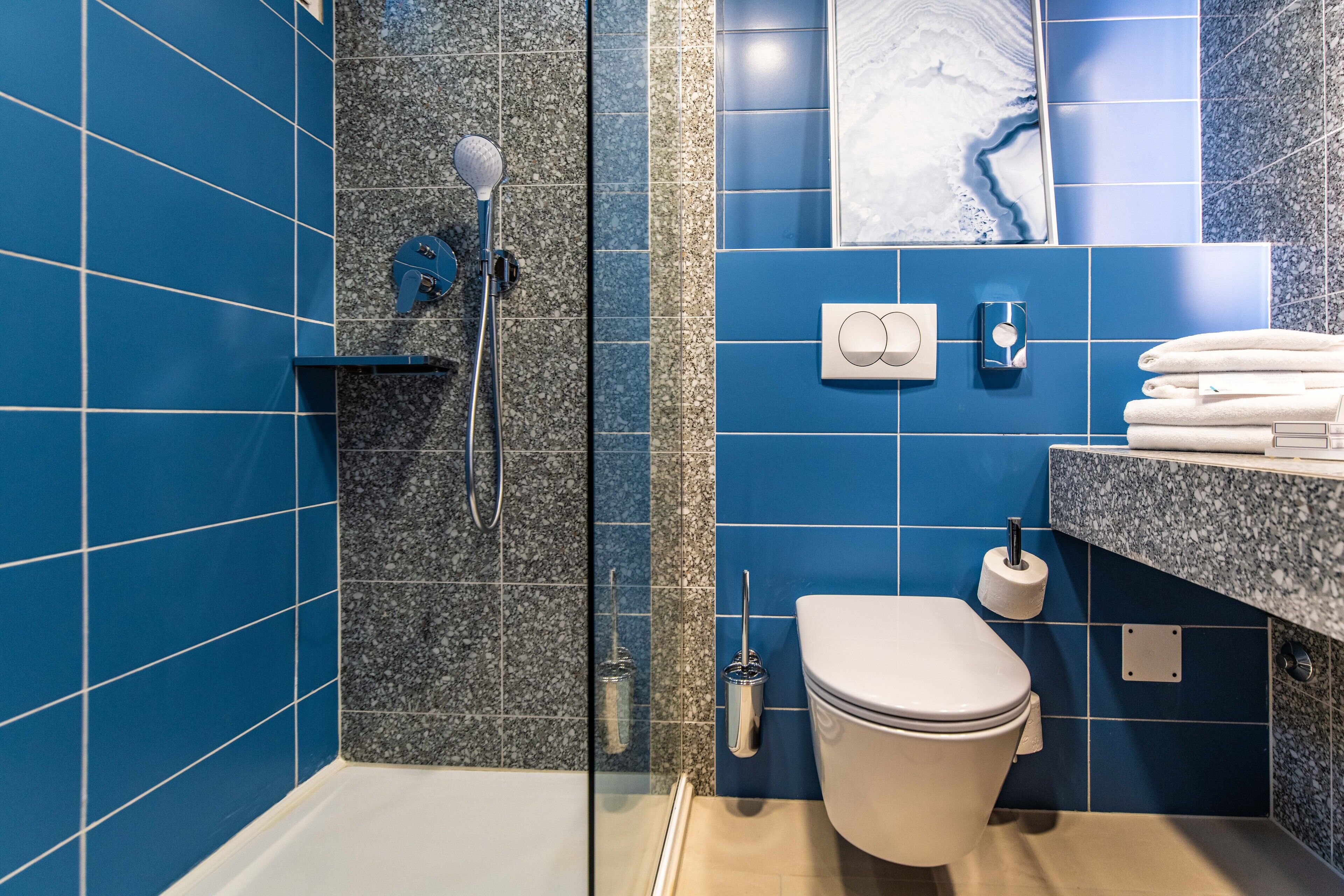A bathroom with blue tiles, a shower, a toilet, and a towel rack.