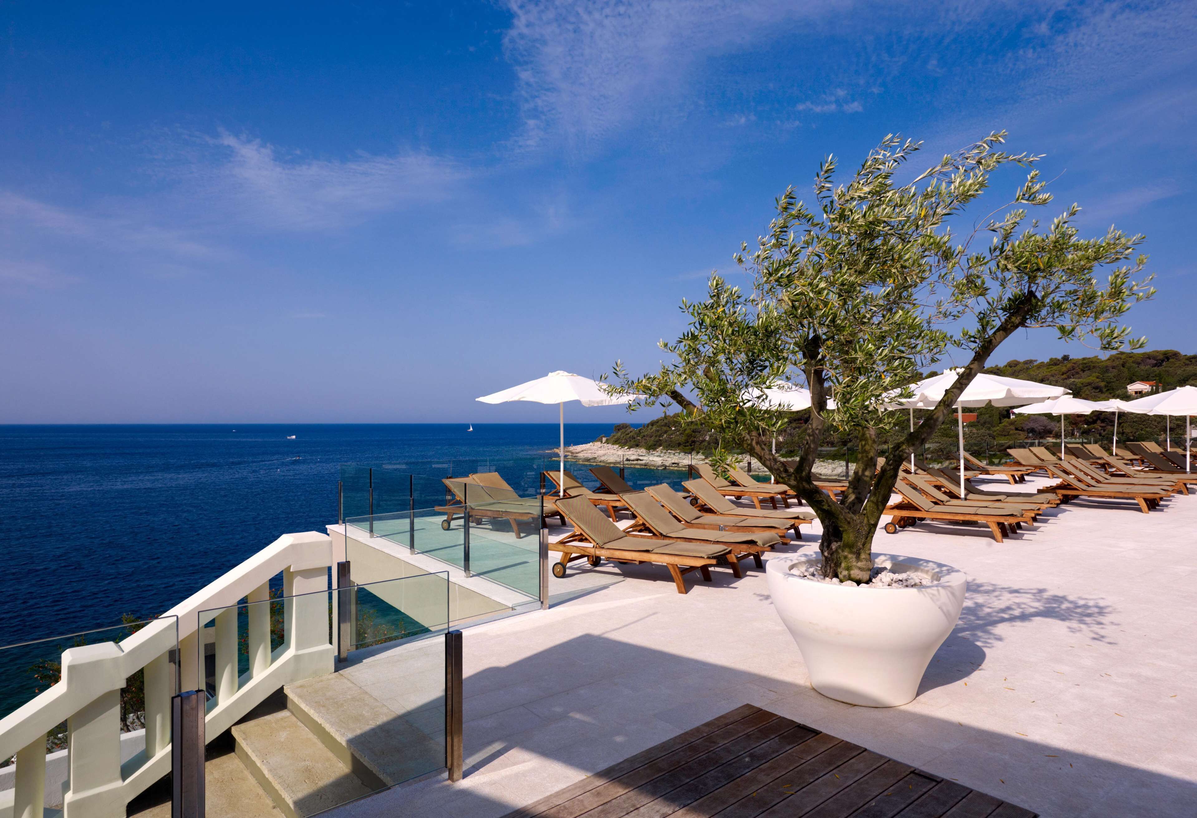 A poolside area with lounge chairs and umbrellas, overlooking the sea.