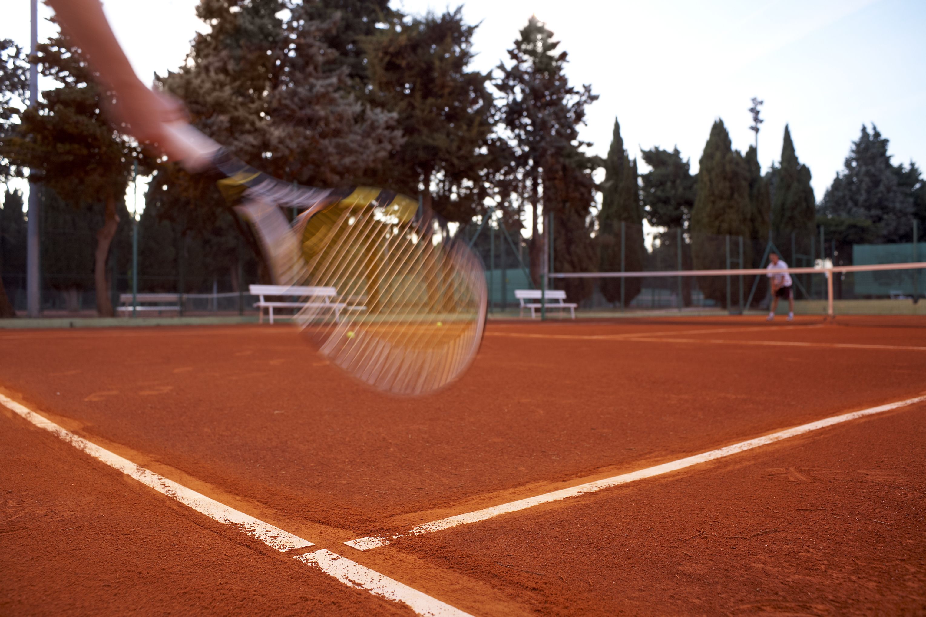 A tennis court with a net, trees, and a bench.