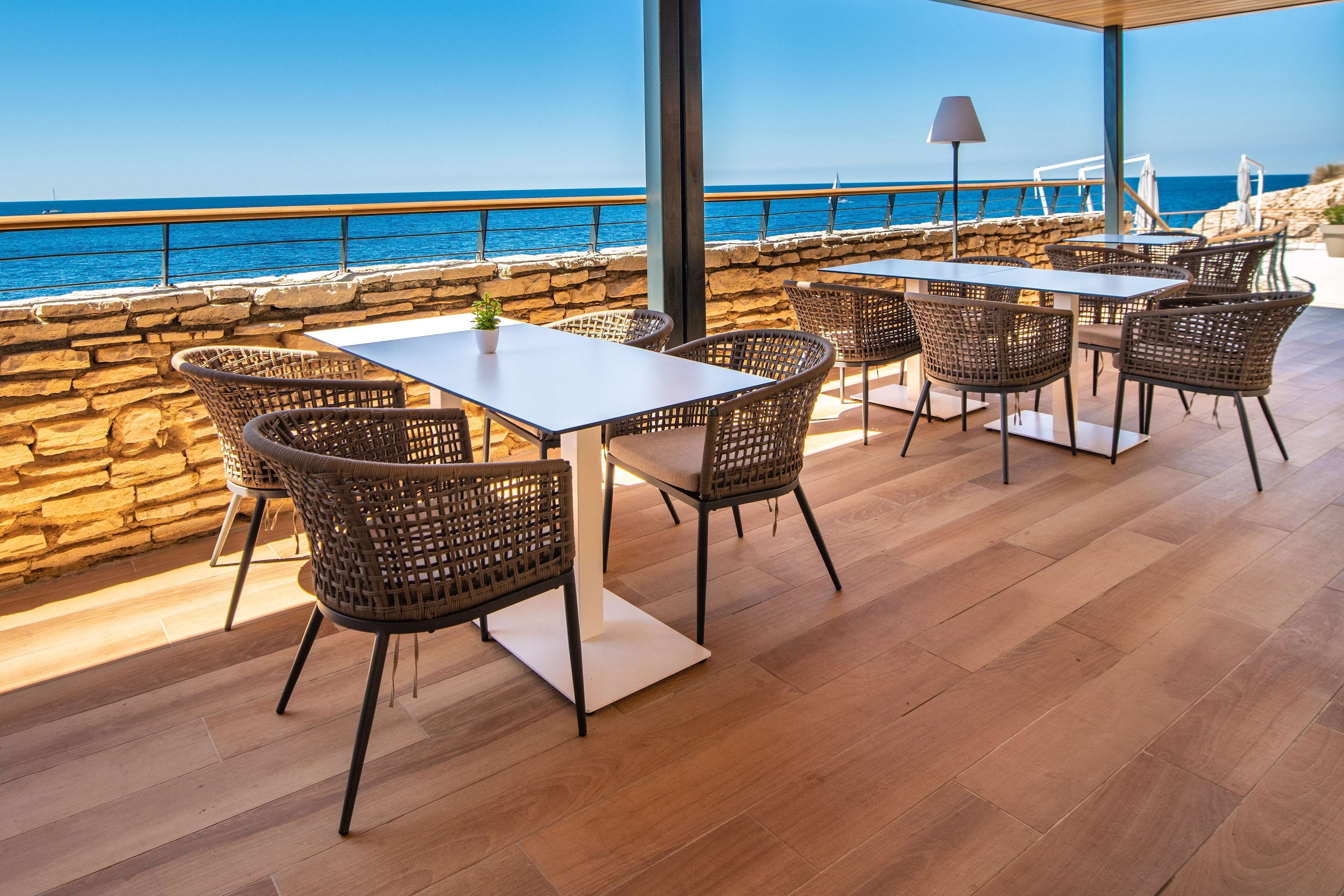 An outdoor patio with a stone wall, wooden flooring, wicker chairs, and a table.