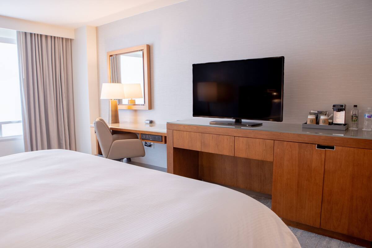 A hotel room with a large bed, a desk with a TV, a lamp, and a coffee maker.