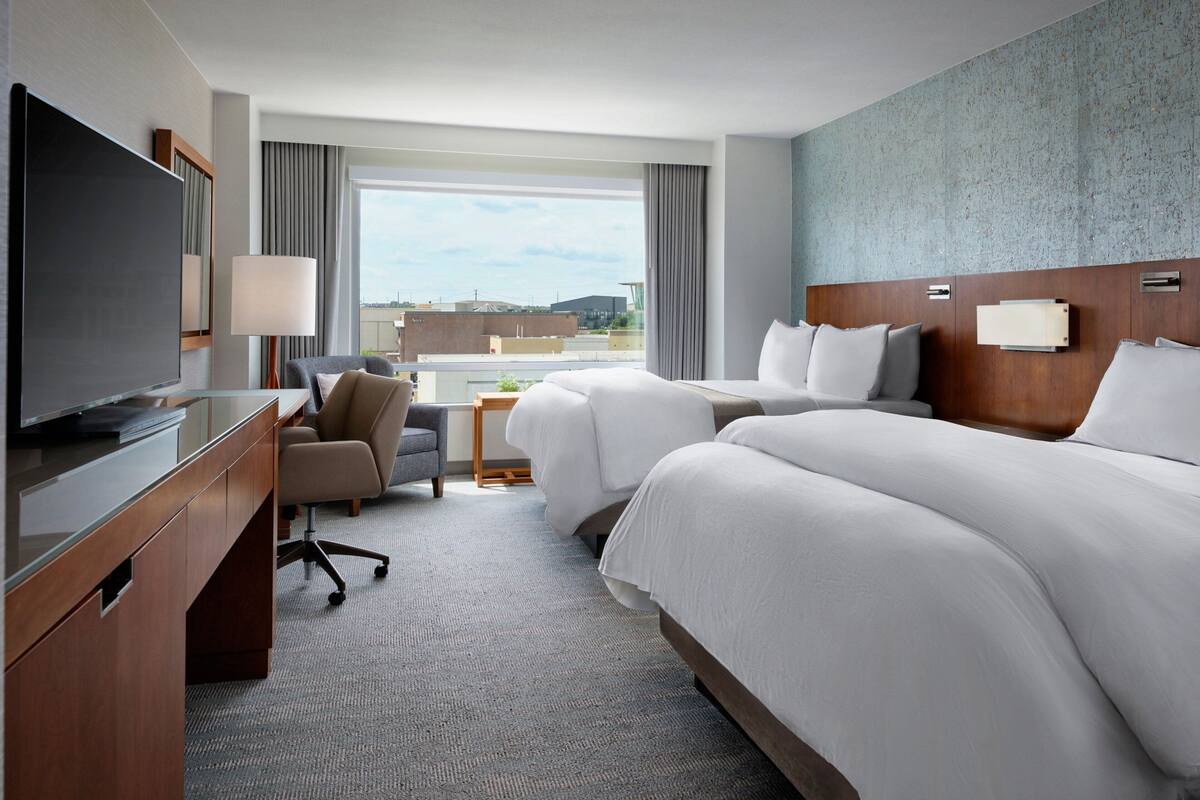 A hotel room with a large bed, a desk with a TV, a chair, and a view of the cityscape.