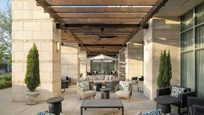 An outdoor patio area with a wooden pergola, seating arrangements including sofas and chairs, and a central round table. - The Westin Austin at The Domain (Austin)