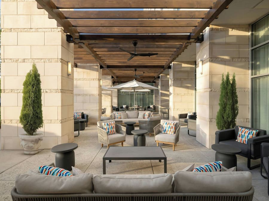 Un patio exterior con un porche de madera, con arreglos de asientos que incluyen sofás y sillones, y una mesa redonda central.
