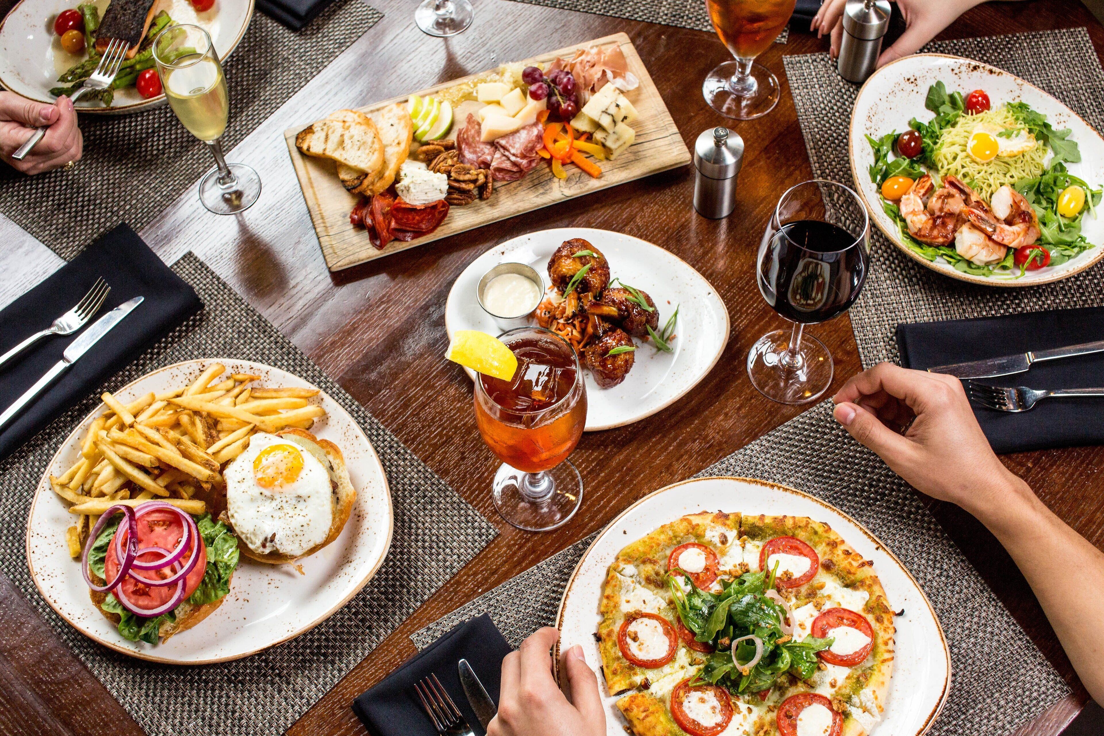 Uma mesa de jantar com diversos pratos, incluindo pizza, salada e um tabuleiro de carnes e queijos.