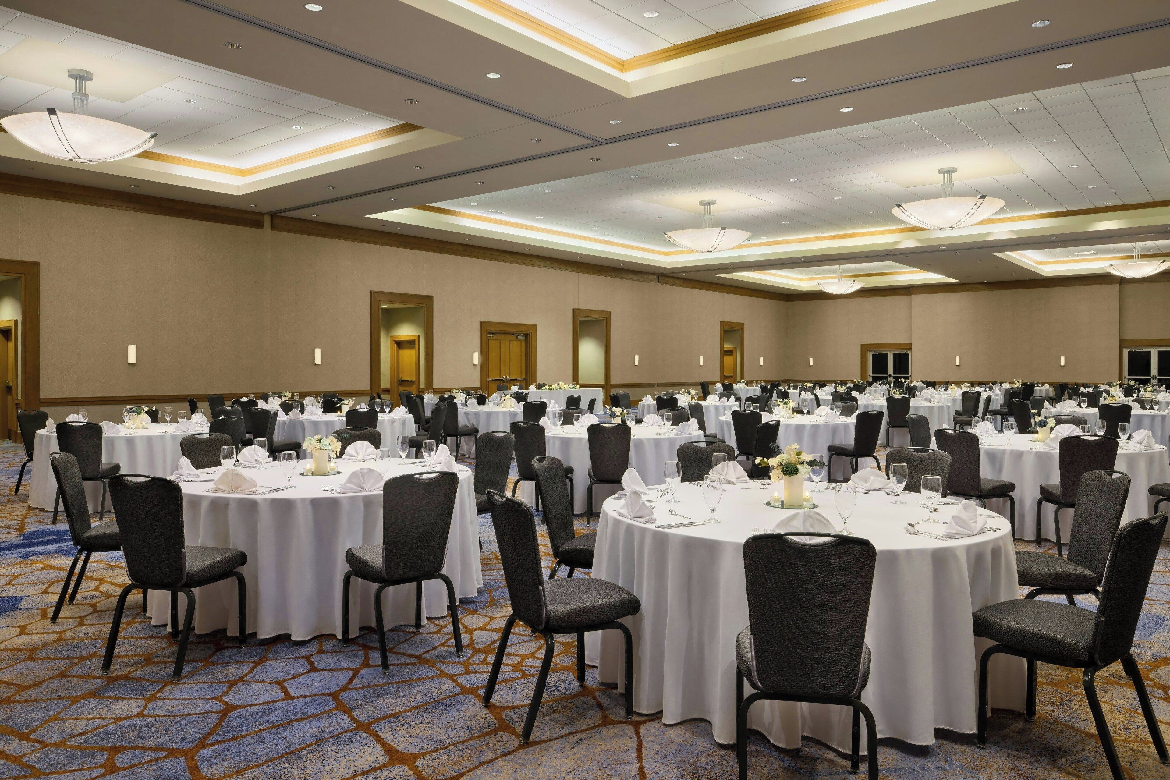 A large banquet hall with round tables set for dining, arranged in rows.