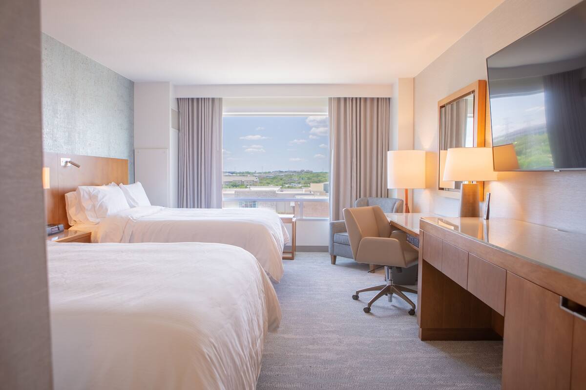 A hotel room with two beds, a desk, a chair, and a TV.