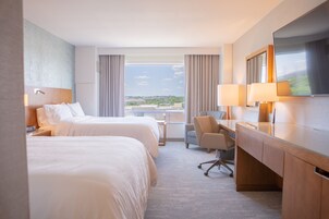 A hotel room with two beds, a desk, a chair, and a TV.