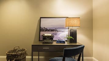 A desk with a typewriter, a lamp, a framed picture, and a chair.