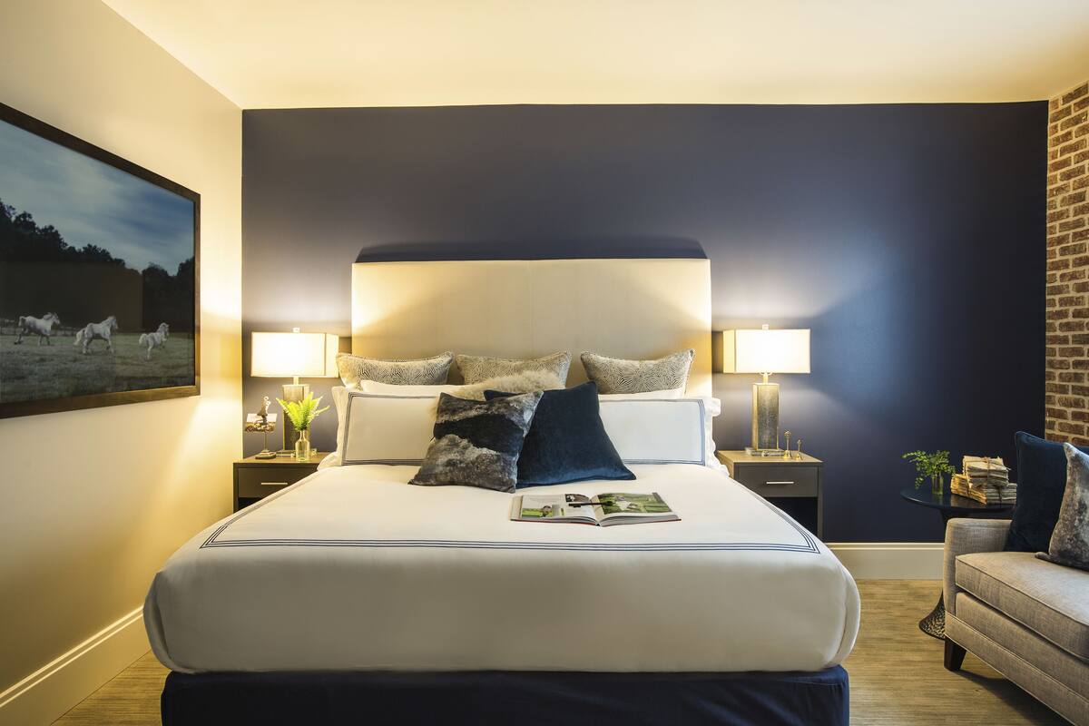 A large bed with a headboard, two bedside tables with lamps, a small side table, and a sofa.