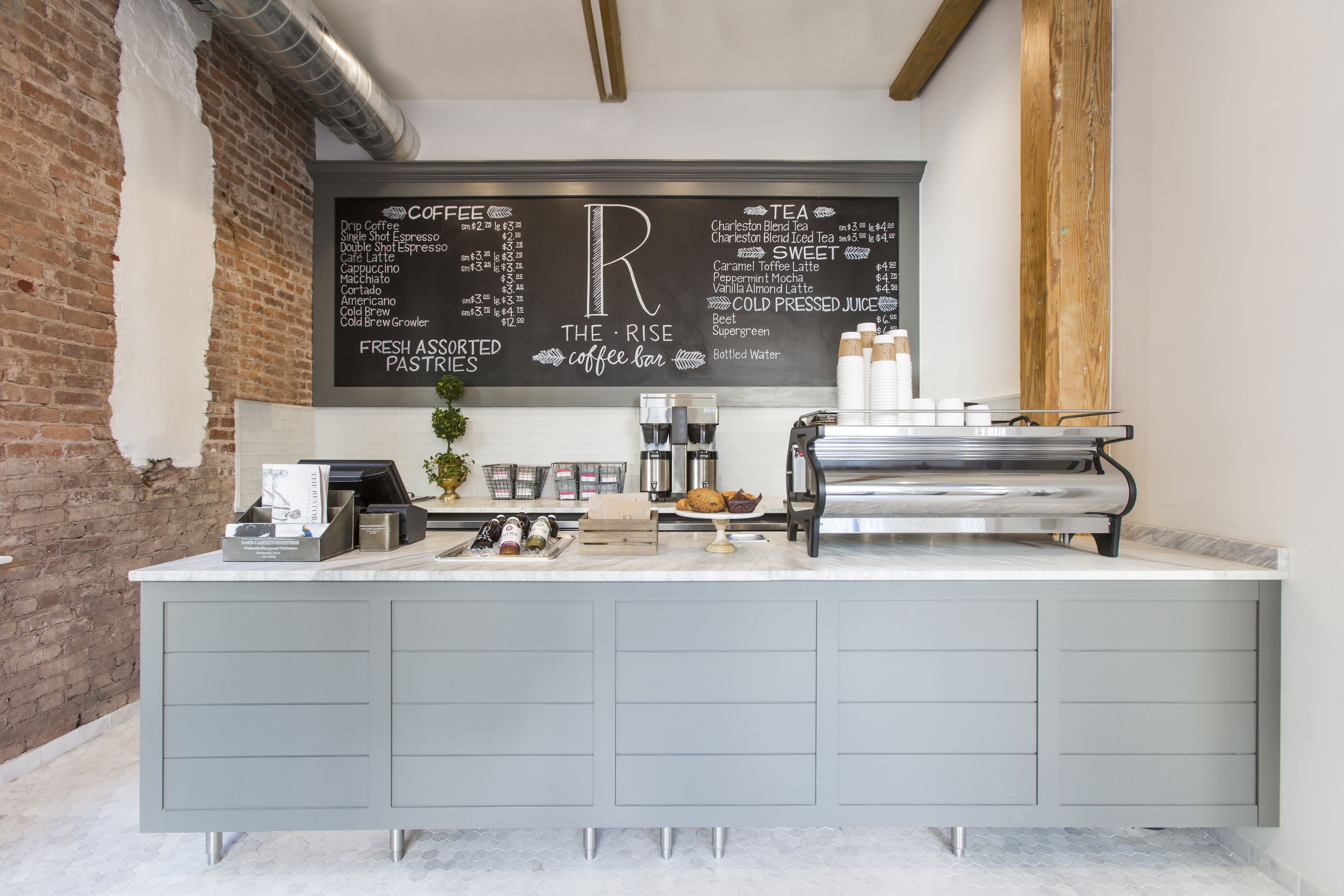 A coffee bar with a menu board listing coffee and tea options, fresh assorted pastries, and a water dispenser.