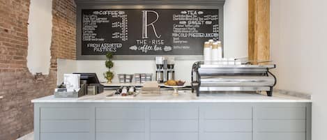 A coffee bar with a menu board listing coffee and tea options, fresh assorted pastries, and a water dispenser.