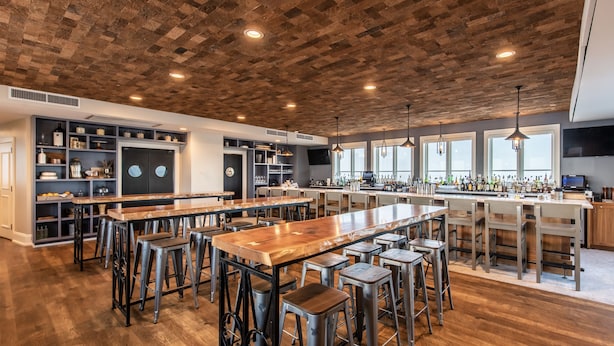 A spacious bar area with high stools, a long wooden bar counter, and a kitchen area with shelves and appliances.