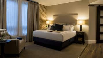 A hotel room with a large bed, two bedside tables with lamps, a chair, and a view of the city through large windows.