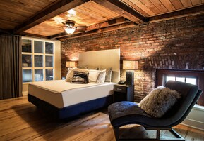 Quarto com uma cama grande, uma cadeira, uma mesinha de cabeceira e uma parede de tijolos.