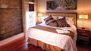A hotel room with a brick wall, a large bed with multiple pillows, a wooden floor, and two bedside lamps.