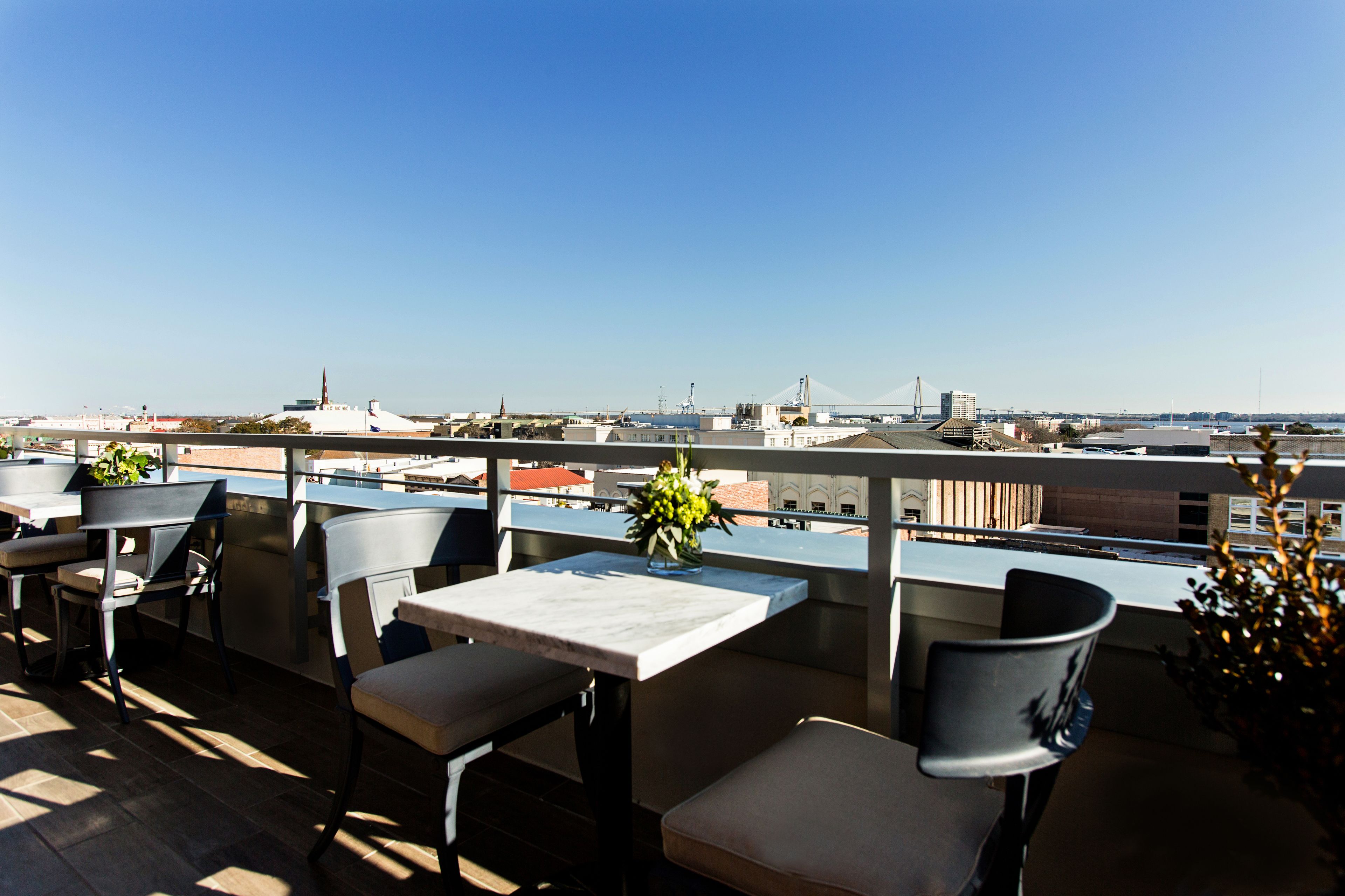 Una terraza en la azotea con mobiliario exterior, una vista despejada del horizonte urbano y un puente a lo lejos.