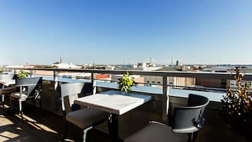 Una terraza en la azotea con mobiliario exterior, una vista despejada del horizonte urbano y un puente a lo lejos.
