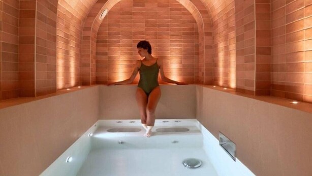 A person in a green swimsuit standing in a spa bath with arched brick walls. - Hotel du Nord et de l'Est (Paris)
