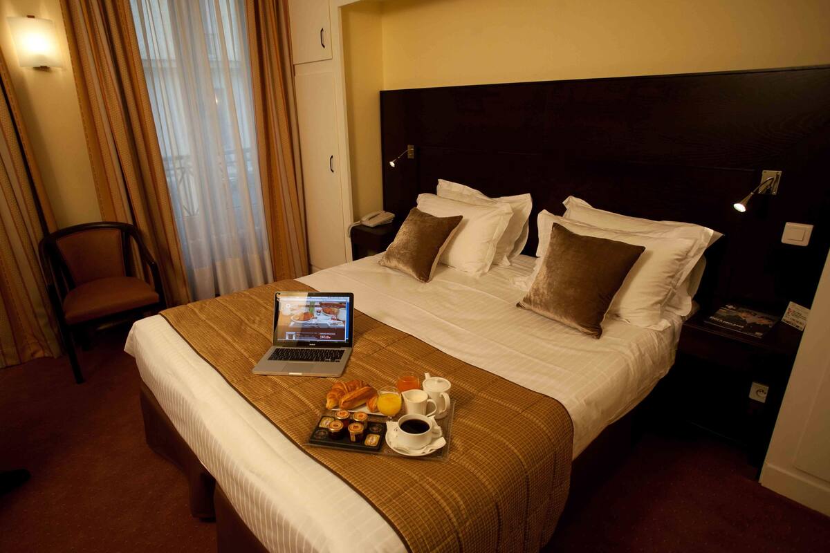 Une chambre d’hôtel avec un lit bien fait, un ordinateur portable, des articles pour le petit-déjeuner et une chaise.