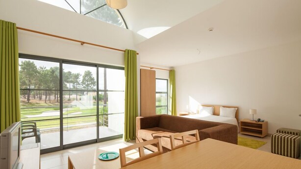 Une chambre d’hôtel moderne dotée d’une grande fenêtre, d’un lit, d’un canapé, d’une table à manger et d’un petit téléviseur.