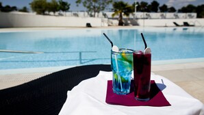 Une table placée au bord de la piscine, avec deux boissons et une nappe blanche.