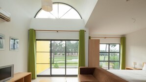 Une chambre d’hôtel moderne dotée d’une grande porte-fenêtre coulissante donnant sur un jardin, d’un canapé, d’une télévision et d’une petite table.