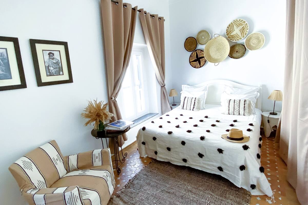 Um quarto com cama, cadeira, mesa de cabeceira e decoração nas paredes.