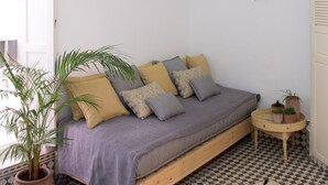 A cozy room with a checkered floor, a wooden bed with a purple blanket, a hanging wicker light, and a small round table with plants.