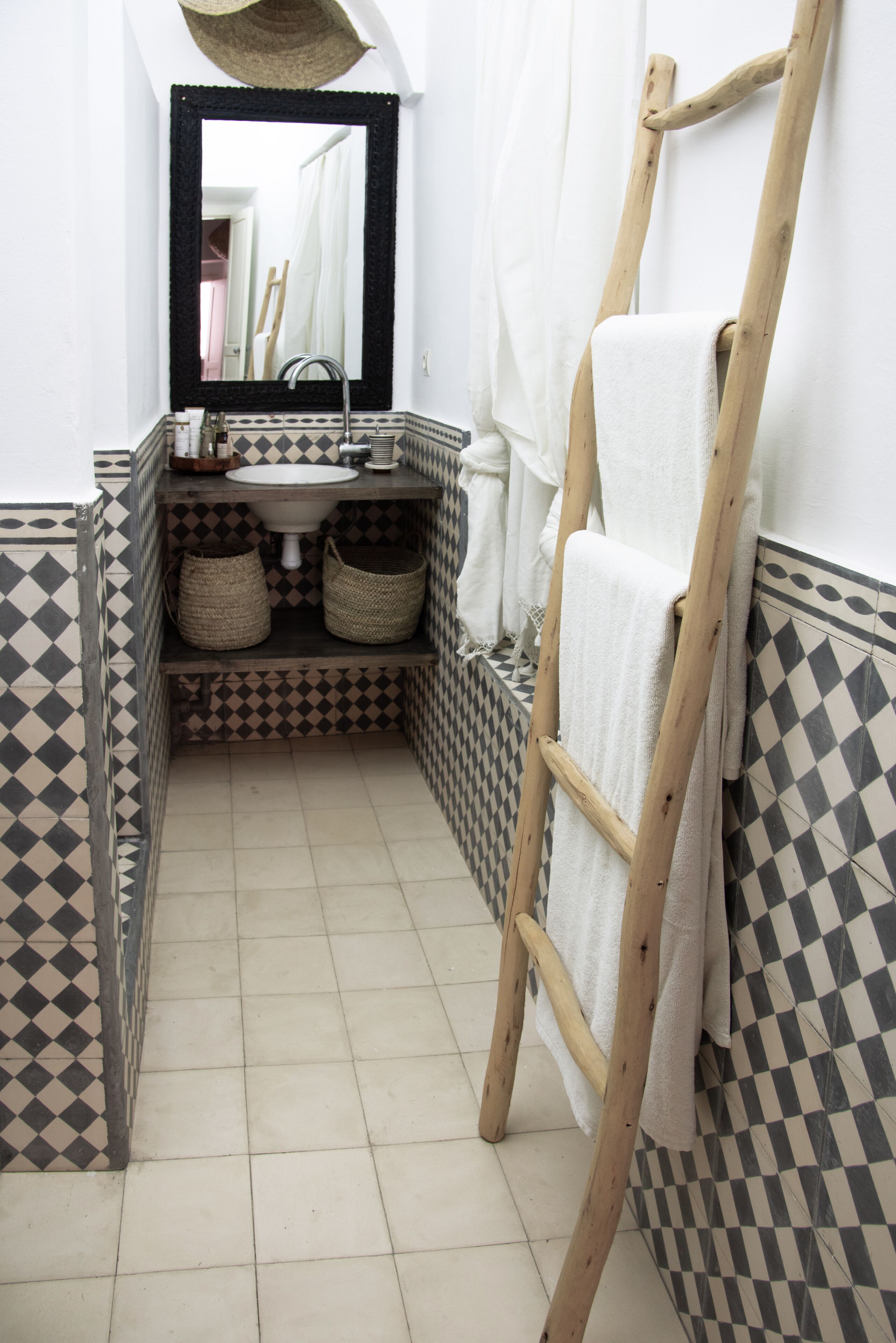 A bathroom with a checkered floor, a wooden ladder, a white sink, and two woven baskets.