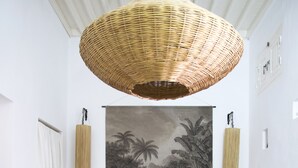 A bedroom with a large bed, a hanging woven light fixture, a tropical-themed wall tapestry, and a checkered floor.
