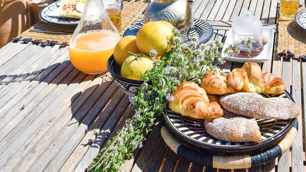 A wooden deck with a breakfast setup including croissants, lemons, and a glass of orange juice.
