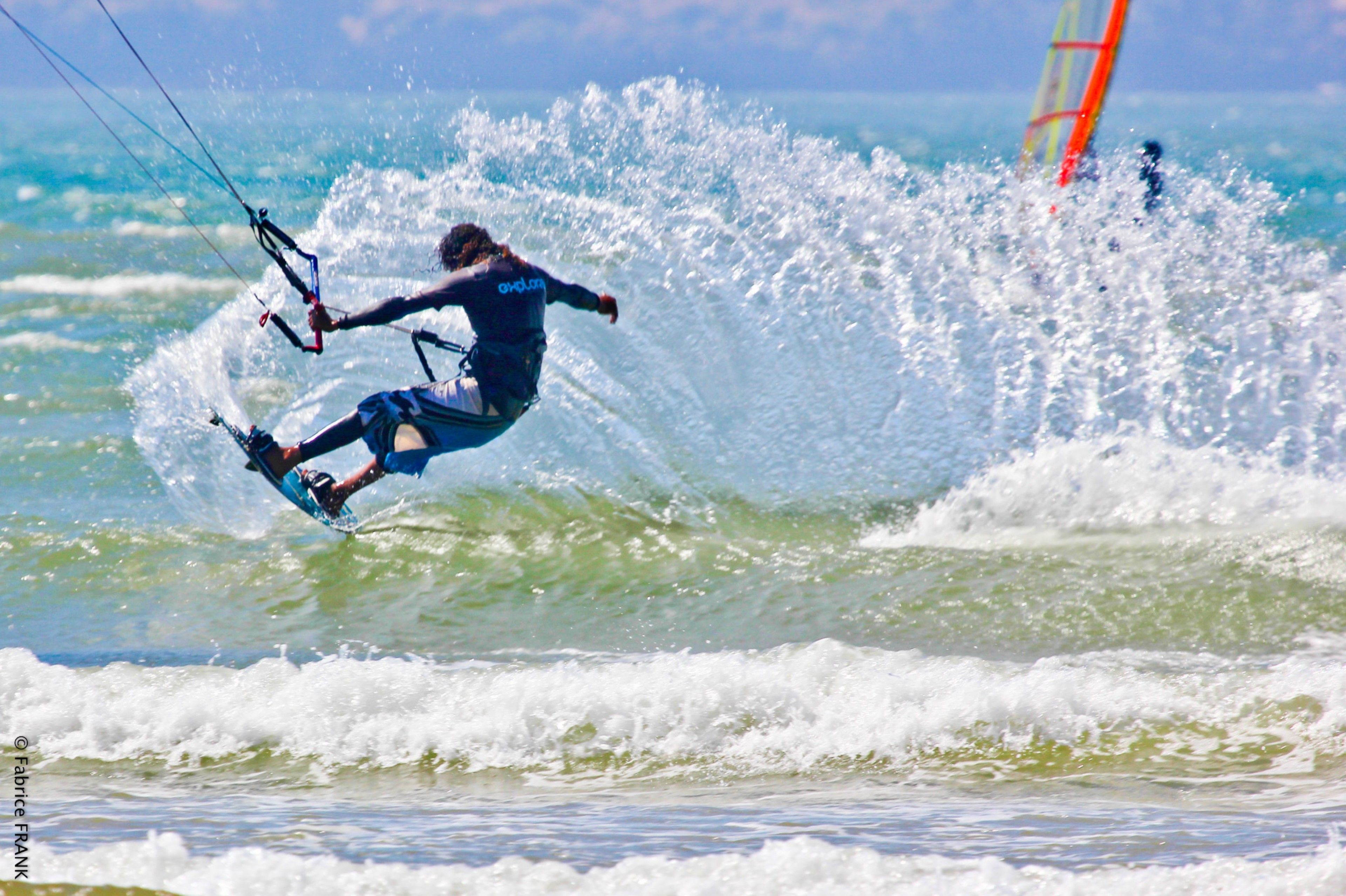A person windsurfing on a wave with a clear sky in the background.