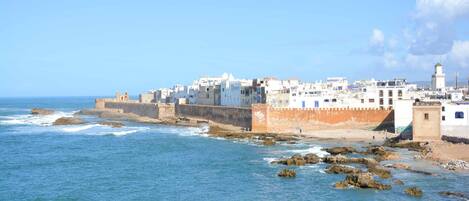 A coastal town with white buildings, a lighthouse, and rocky shoreline.
