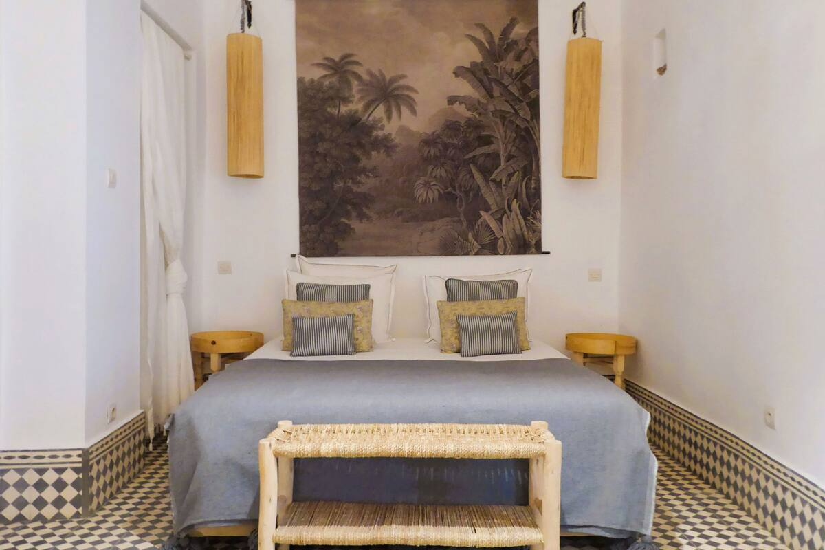 Quarto com cama, almofadas, tapeçaria pendurada e chão xadrez.