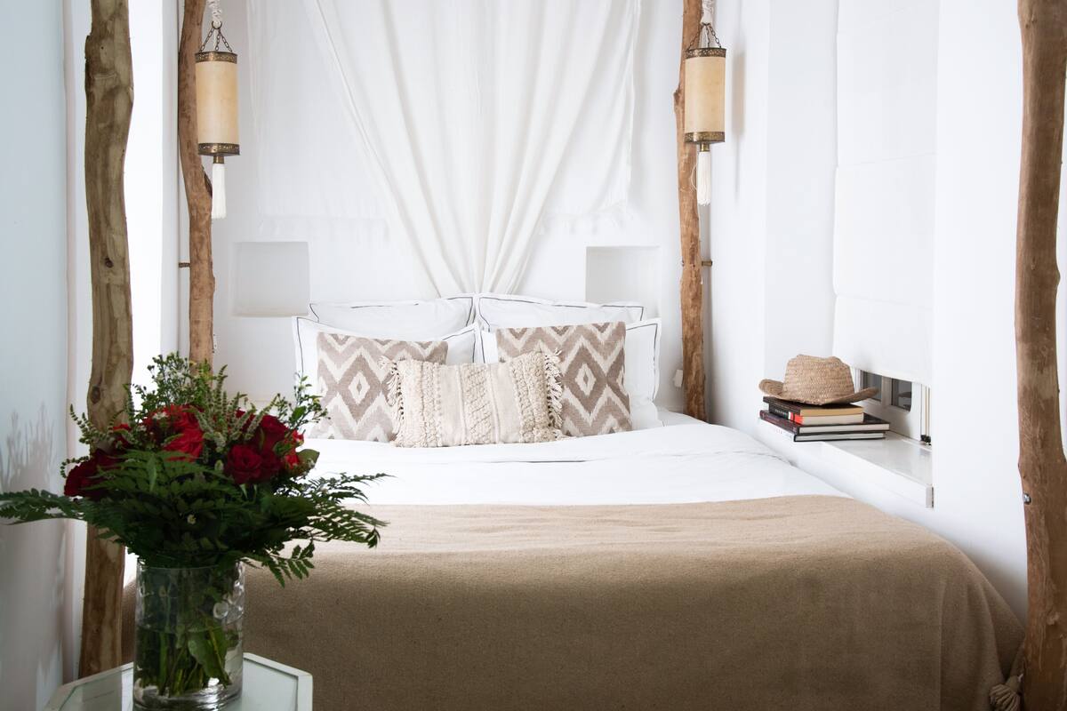 Quarto bem arrumado com cama, mesa de cabeceira e um vaso de flores.