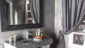 A bathroom with a large mirror, dark curtains, a sink with toiletries, and woven baskets.