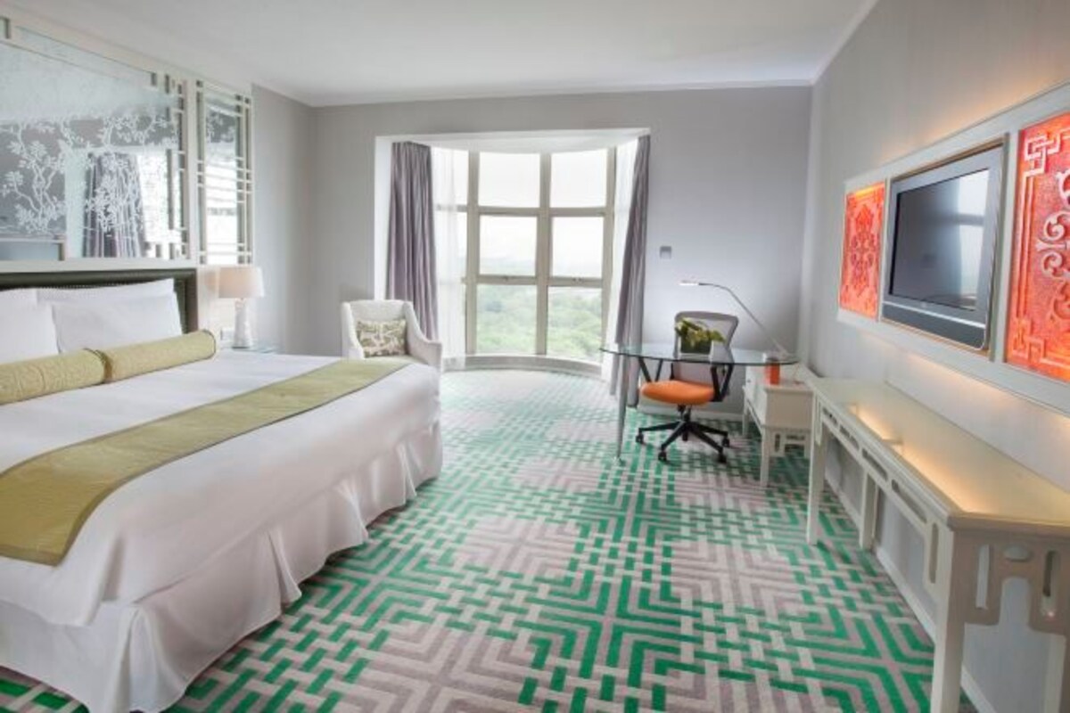 A hotel room with a large bed, a desk with a chair, a television, and a window with curtains.