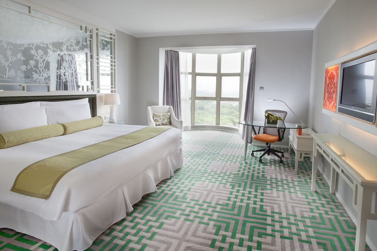 Habitación de hotel con una cama grande, un escritorio, una silla, un televisor y una ventana con cortinas.