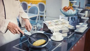 A chef cooking an omelette on an induction stove in a modern kitchen with a buffet setup in the background. - Dorsett Shanghai (Shanghai)